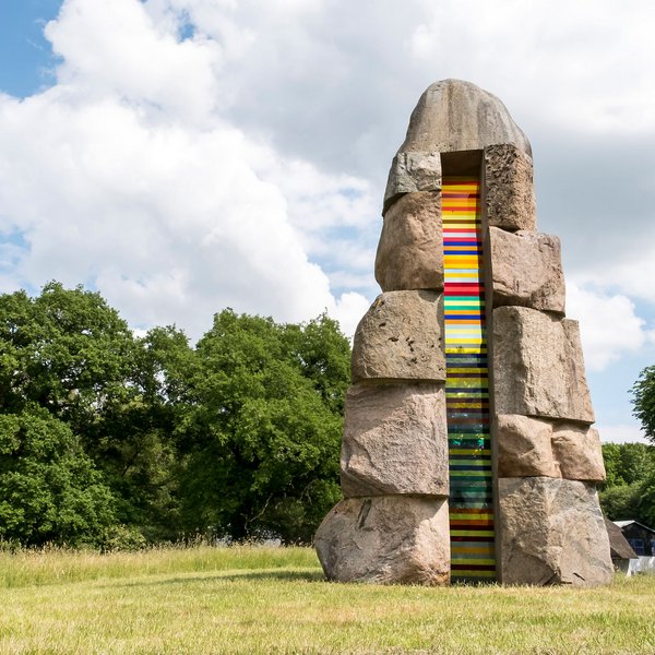 Kunst & Kultur (© MHT.SH & Peter Lühr) Bunte Steinskulptur auf einer grünen Wiese.
