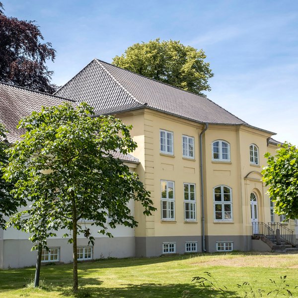 Denkmäler (© Mittelholstein.de / Peter Lühr) Ein herrschaftliches gelbes Haus umgeben von grünen Bäumen. Der Himmel ist blau, die Sonne scheint.