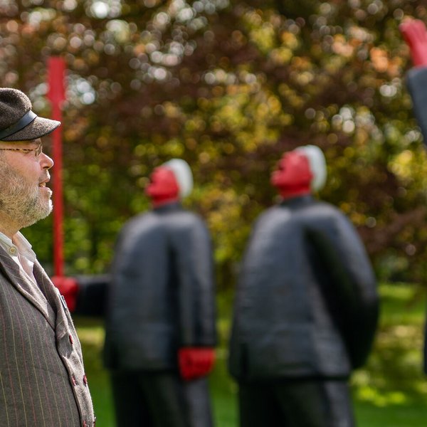 Tipps für einen Kurzurlaub (©sh-tourismus.de/MOCANOX) Ein Mann steht vor einer Kunstinstallation. menschliche Figuren stehen im Hintergrund, die Natur ist grün.
