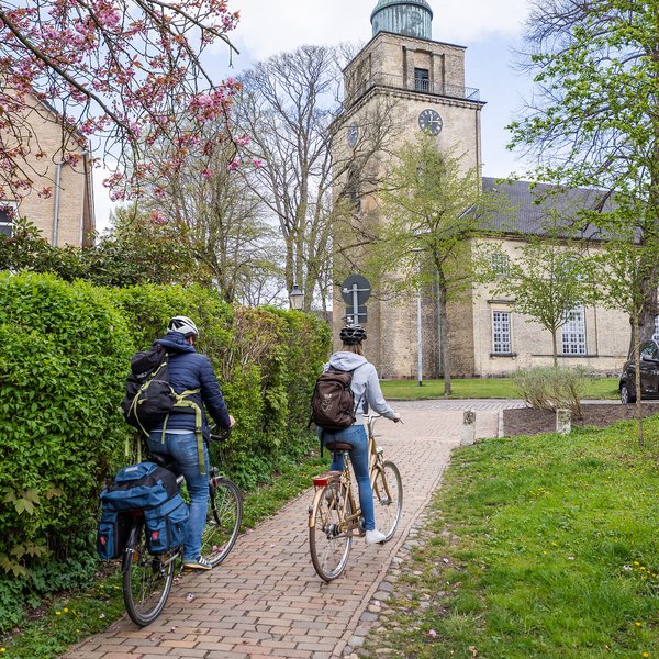 Ausflugstipps (© sh-tourismus.de/MOCANOX) Zwei Radfahrer fahren im Frühling auf eine Kirche zu.