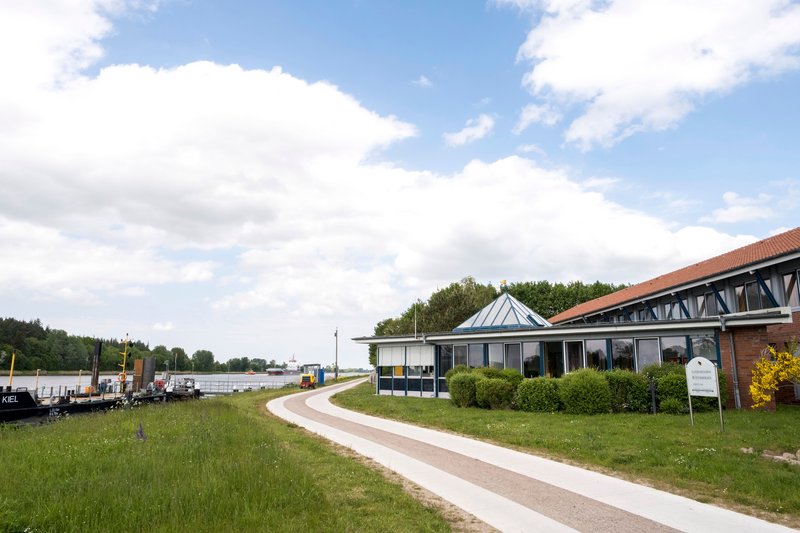 Gebäude der Lotsenstation Rüsterbergen am Ufer eines Kanals mit einem Weg im Vordergrund.