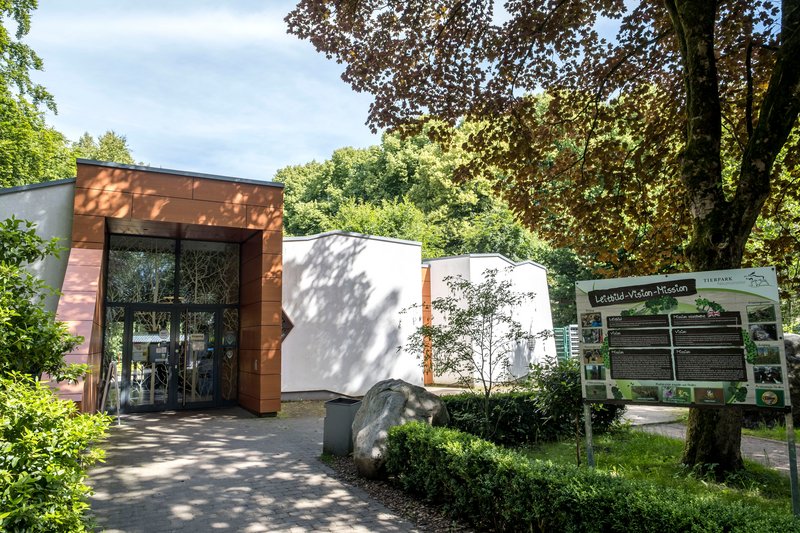 Eingangsbereich des Tierparks Neumünster mit Informationsschild und umgebender Natur.
