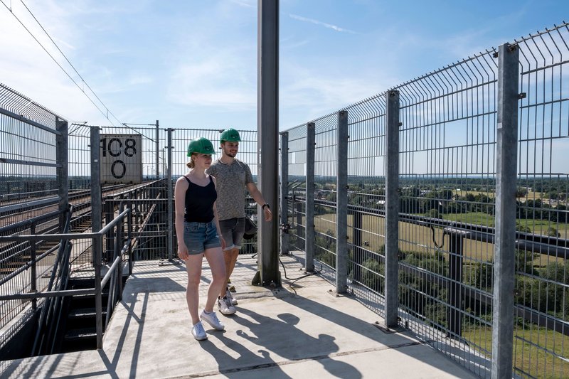 Zwei Personen mit grünen Helmen auf einer Aussichtsplattform der Eisenbahnhochbrücke Rendsburg.